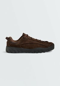 Baskets en daim brun foncé avec semelle noire robuste, design bas, fermeture à lacets et col matelassé sur un fond clair uni.
