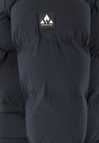 Marineblaue Steppjacke mit gesteppten Abschnitten, ausgestattet mit einem quadratischen schwarzen Aufnäher mit einem weißen Berglogo und dem Wort "WHISTLER". Angenehme Textur.
