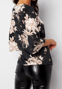 Blusa negra con flores rosas y crema, mangas tres cuartos y un escote redondo, combinada con pantalones de cuero vegano negro brillante.