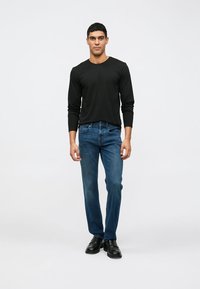 Maglietta nera a maniche lunghe, jeans blu e scarpe nere. Design slim-fit, gamba dritta, denim lavato di media intensità con minima scoloritura, texture liscia.