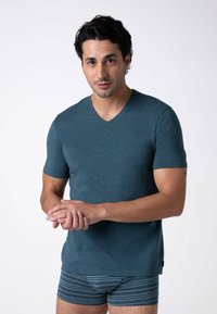 T-shirt a V verde acqua realizzato in tessuto morbido, maniche corte, design aderente. Abbinato a pantaloni da boxer a righe. Modello mostrato su sfondo neutro.