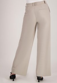 Beige wijde broek met een gladde textuur, voorzien van een ceintuurlint in de taille en zijzakken. Gecombineerd met zwarte hoge hakken.