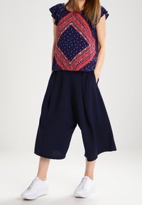 Marineblå cropped vide bukser parret med en mønstret kortærmet top med et rødt og hvidt diamantmønster. Hvide sneakers fuldender looket.