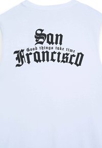 Maglietta bianca senza maniche con bold testo nero che recita "San Francisco" e la frase "Le cose buone richiedono tempo" in caratteri ornamentali.