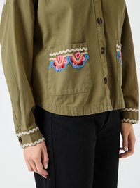 Olivenfarget knapp-up skjorte med broderte lommer som har rosa, røde og blå blomsterdesign; kontrasterende bølgekant på mansjettene.