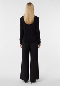 Schwarzes Langarmoberteil mit tailliertem Design, kombiniert mit weit geschnittenen schwarzen Hosen. Glatte Textur, minimale Details und klassischer Schnitt.