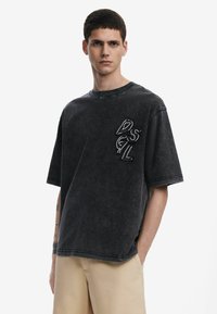 Camiseta de denim negro de gran tamaño con un escote redondo y mangas cortas. Presenta un logotipo texturizado 'DSGL' en el pecho en un color contrastante.