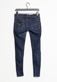 Jeans ajustados de denim azul oscuro con acabado mate. Presenta dos bolsillos traseros con costuras decorativas y una cremallera en la parte delantera.