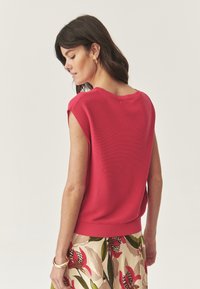 Maglione a maniche corte e a coste di un vivace colore rosa, con scollatura a V e una vestibilità morbida, abbinato a una gonna con stampa floreale.
