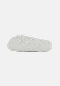 Suola di sneaker bianca con motivi testurizzati, caratterizzata da un logo rotondo, bordi scanalati e un design di trazione unico. Materiale resistente.