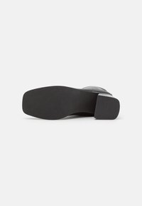 Talons en cuir noir avec une finition texturée. Bout carré et talon bloc. Semelle lisse avec un minimum de détails.