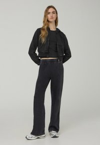 Felpa corta nera con tasca frontale, abbinata a pantaloni della tuta neri con gamba larga, dotati di vita con cordino e cuciture a contrasto. Sneakers argentate.