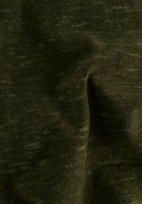 Tissu polaire doux vert foncé avec une surface texturée et duveteuse et des plis visibles créant des ombres douces.