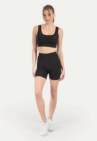 Schwarzes sportliches Crop-Top kombiniert mit hoch taillierten schwarzen Shorts. Glatter, dehnbarer Stoff mit minimalen Nähten und körperbetontem Schnitt.