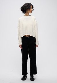 Bílý texturovaný krátký svetr v kombinaci s černými kalhotami s širokými nohavicemi a černými kozačkami. Oblečení má pohodlný střih a minimální zdobení.