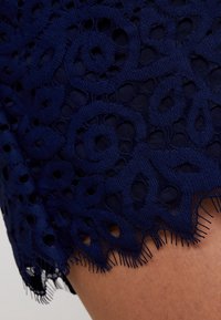 Námořnická modrá krajka s květinovými a geometrickými výřezy na pokožce, s vroubkovaným a třásňovým okrajem.