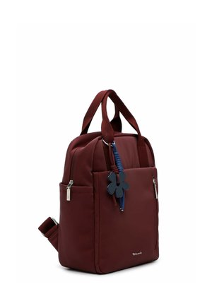 Compacte bordeaux rugzak met dubbele handvatten, voorzakken met rits en een decoratieve blauwe bloemen sleutelhanger die aan een handvat hangt.