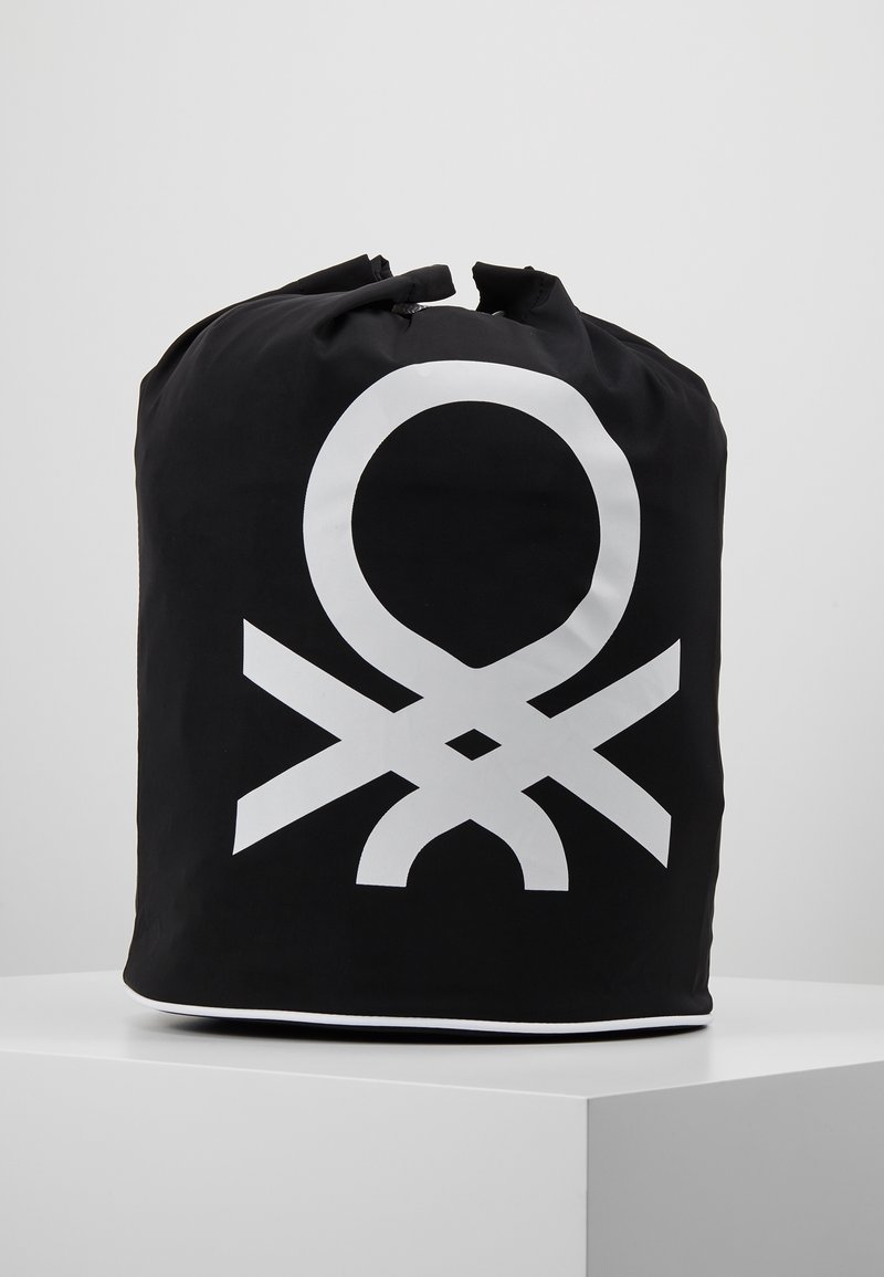 Sac noir de forme cylindrique, arborant un motif graphique blanc distinctif. Fabriqué en matériau durable, il dispose d'une fermeture à cordon en haut.