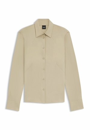 Camicia beige a maniche lunghe con bottoni, caratterizzata da un colletto appuntito, cuciture sulle spalle e orlo curvo. Tessuto liscio con una leggera lucentezza e vestibilità sartoriale.