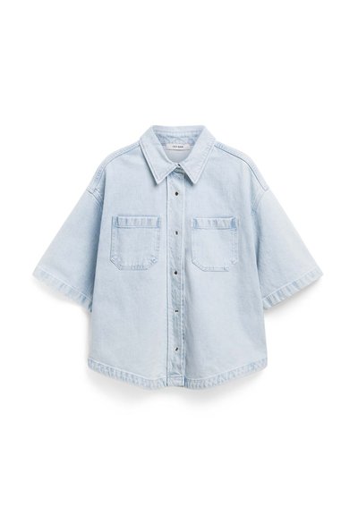 Camicia in denim azzurro chiaro con maniche corte, colletto a punta, chiusura con bottoni e due tasche sul petto. Presenta una vestibilità rilassata e un orlo leggermente arrotondato.