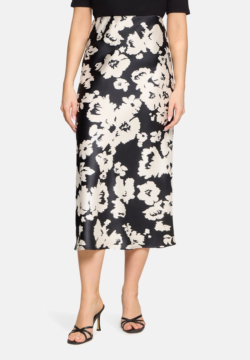 Sort satin midi-nederdel med stort hvidt abstrakt blomsterprint, stylet med sorte, snørede høje hæle, vist fra talje til fødder.