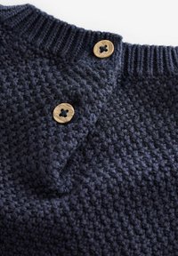 Granatowy sweter wykonany na drutach z fakturowanym wzorem, z prążkowanym dekoltem i dwoma jasnymi drewnianymi guzikami po jednej stronie.