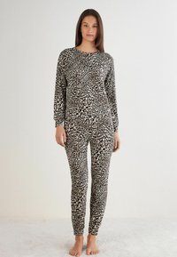Loungewear-Set im Leopardenmuster, bestehend aus einem Langarmoberteil und einer eng anliegenden Hose, aus weichem Material mit glatter Textur. Gemustert in Schwarz und Beige.