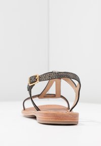 Zwarte stoffen sandaal met een gouden gesp, open achterkant, platte houten zool en een gestructureerde band. Ontworpen met minimalistische details.