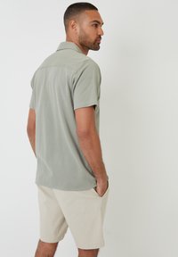 Camisa polo de manga corta en gris claro con cuello, combinada con pantalones cortos beiges. Diseño casual con una textura suave y un corte clásico.