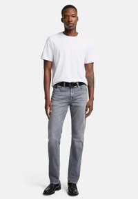 Jeans in denim grigio con taglio dritto, abbinati a una t-shirt bianca semplice e una cintura nera. Il look è completato da scarpe nere.
