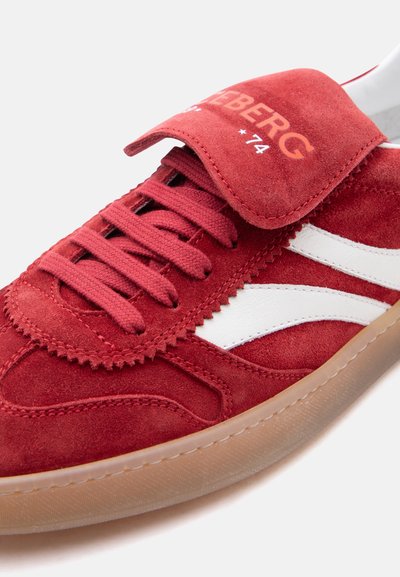 Baskets en daim rouge avec des bandes blanches sur les côtés, des lacets rouges assortis, une semelle en gomme et une bride à velcro portant l'étiquette "ICEBERG *74".