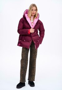 Bordowa kurtka puchowa z różowym podbiciem i kapturem, z zapięciami na napy. Zestawiona z spodniami w panterkę i czarnymi butami na platformie.