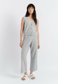 Top grigio senza maniche con bottoni e orlo a costine abbinato a pantaloni grigi a gamba larga, tutto in tessuto morbido. Presenta sandali bianchi.