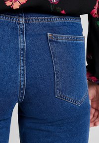 Blå denimjeans med hög midja, som har en enda bakficka. Synlig sömnad i en ljusare nyans kompletterar designen.