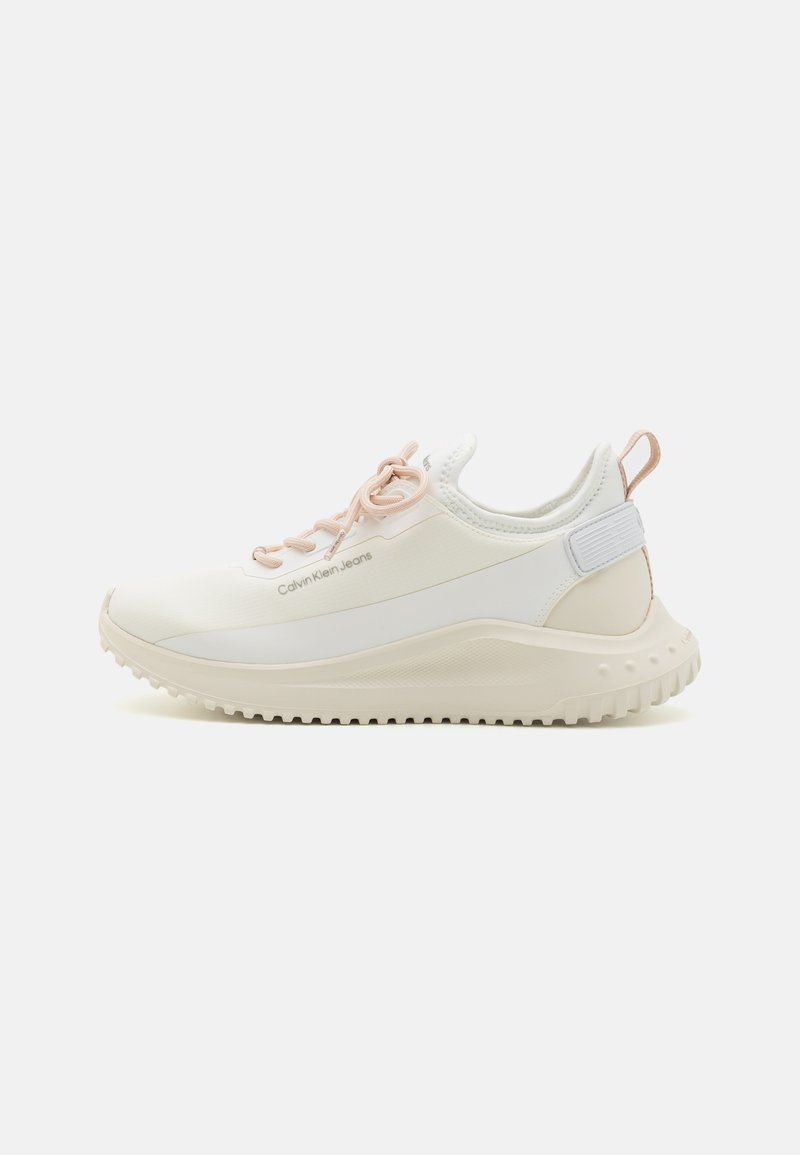 White sneakers with a textured sole, soft pink laces, and branded side detail. Features a smooth upper and cushioned heel for comfort.