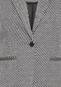 Blazer a righe in bianco e nero con colletto a revers, chiusura con un bottone singolo e due tasche frontali. Tessuto lavorato con dettagli scintillanti.