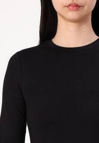 Schwarzes Langarmoberteil mit rundem Ausschnitt, aus glattem, elastischem Material, das eine figurbetonte Silhouette und saubere Nähte aufweist.
