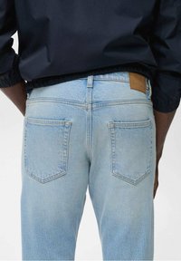 Vaaleansiniset farkut suoralla leikkauksella, joissa on kaksi takataskua ja ruskea nahkainen merkki vyötäröllä. Pehmeä, haalistunut pinta.