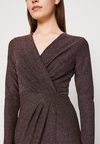 Robe à manches longues de couleur violet foncé avec un éclat métallique, présentant un décolleté croisé, une taille froncée et des plis structurés. Tissu doux et texturé.