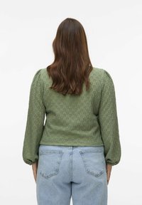 Blusa verde a trama con maniche a sbuffo, corpetto aderente e lunghezza cropped, abbinata a jeans in denim azzurro chiaro.