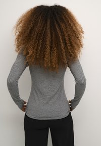 Långärmad topp med svartvita horisontella ränder, figurnära design och stretchy tyg, bärs med svarta byxor.
