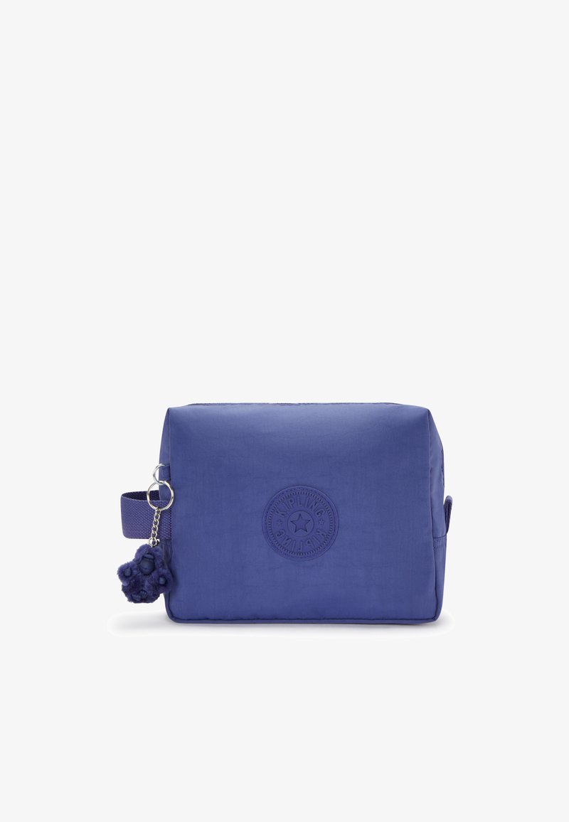 Sac en nylon violet de forme rectangulaire, avec un logo en relief et une poigné latérale. Présente une surface texturée et un pendentif en pompon en fourrure.