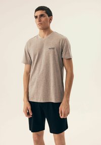 Szary t-shirt z dekoltem w serek, wykonany z miękkiego materiału, z krótkimi rękawami, z małym granatowym logo na klatce piersiowej; noszony z czarnymi szortami.