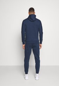Navyblå hoodie och joggingbyxor i mjukt tyg; har en huva, ribbade muddar och en tapered leg-design.