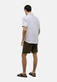 Chemise en lin gris clair à manches courtes avec une coupe décontractée, associée à un short vert foncé et des sandales noires, présentant un design sobre et une texture douce.