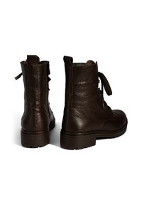 Donkerbruine leren veterschoenen tot de enkel met trek-uitsparingen, een gestructureerd oppervlak en dikke rubberen zolen, te zien van achter en opzij op een witte achtergrond.