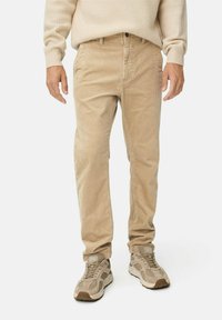 Beige corduroy pants with a relaxed fit, featuring front pockets and subtle vertical ridges. Paired with beige and gray sneakers.