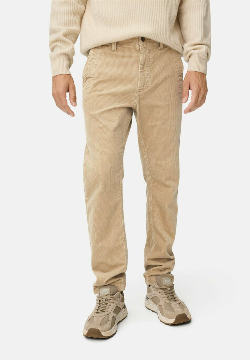 Beige corduroy pants with a relaxed fit, featuring front pockets and subtle vertical ridges. Paired with beige and gray sneakers.