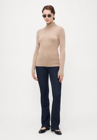 Beige turtleneck sweater made of soft fabric, paired with dark blue flared jeans, and black patent leather shoes. Accessories include sunglasses.