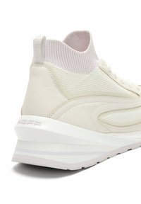 Zapatillas de color claro con cuerpo de cuero liso, cuello tipo calcetín tejido y suela acolchada con una sutil marca.